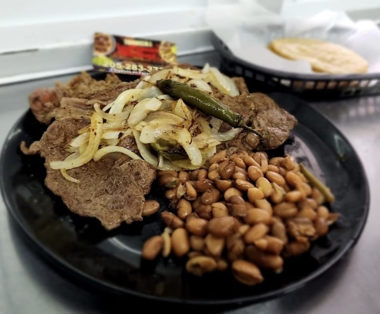 Bisteak Encebollado — grilled steak with caramelized onions, jalapeño, and refried beans